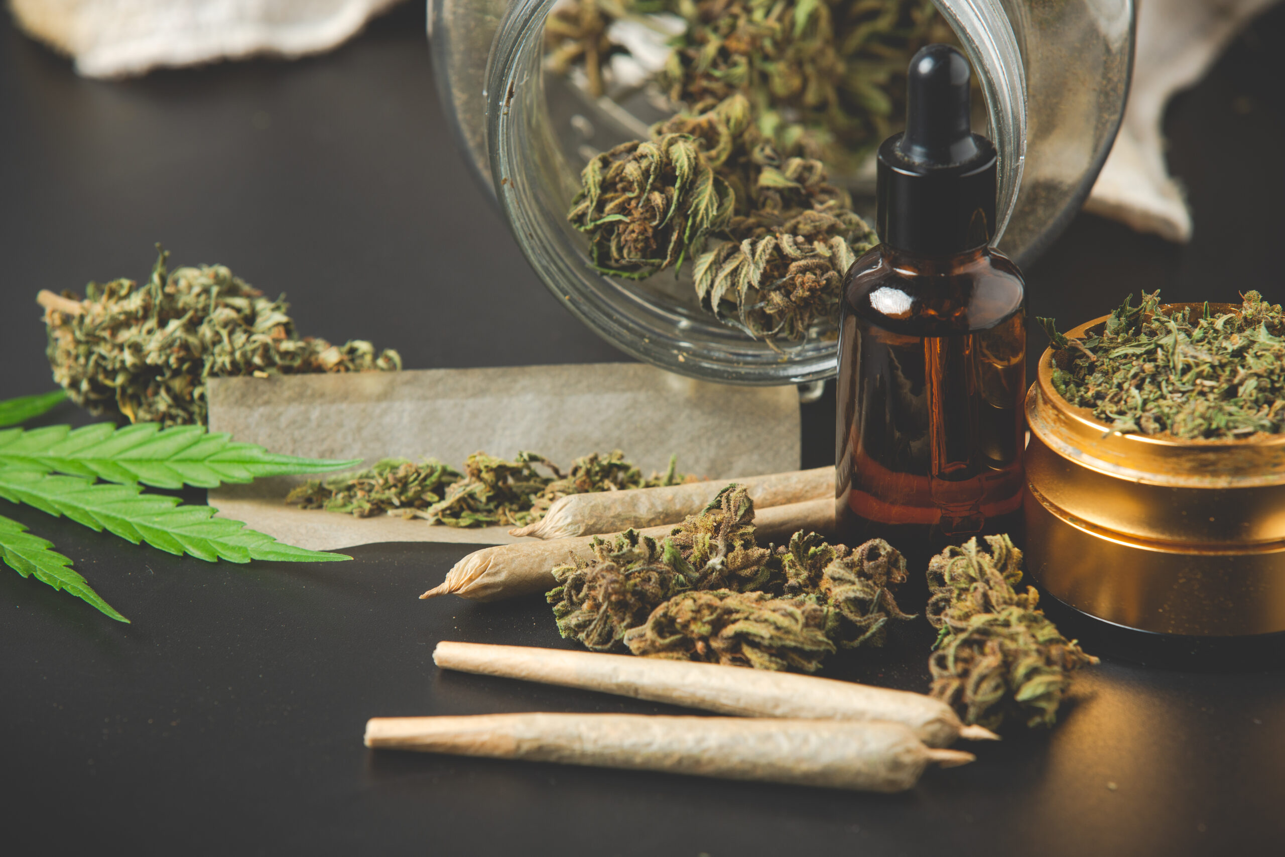 Marihuana / Cannabis in verschiedenen Varianten. Cannabisblatt, Öl, Knospen und Joints liegen auf dem Tisch.